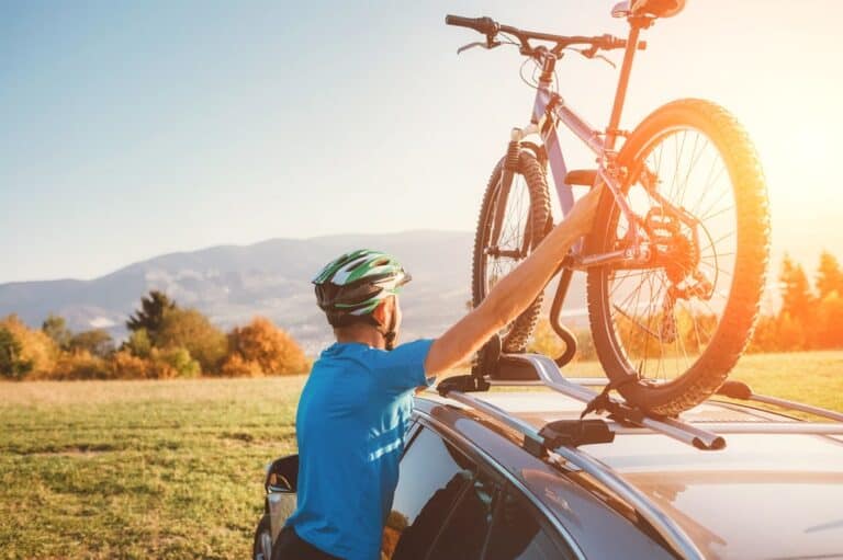 A man fixing his bike onto the rack on top of his car.