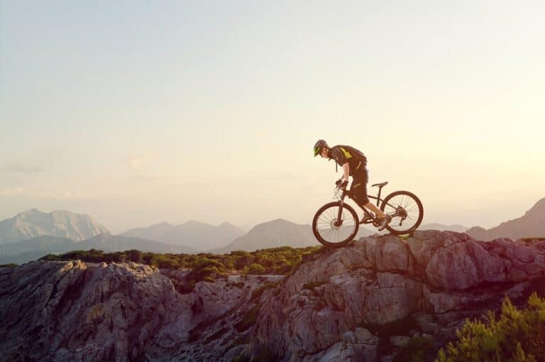 A mountain biker in full gear looking down the rock cliff.