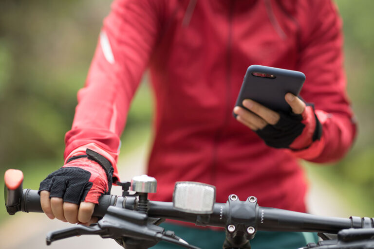 A woman holding a smartphone riding a mountain bike.