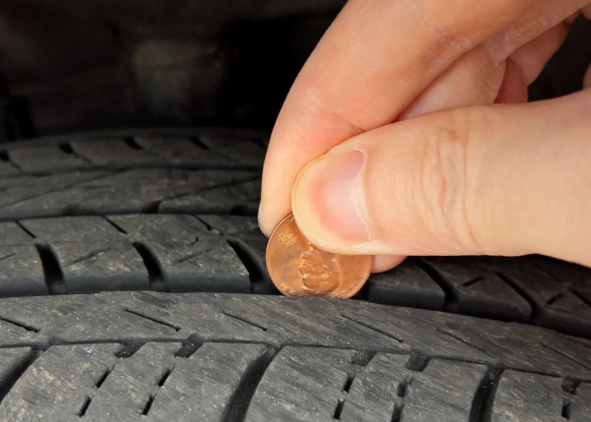 A man placing a penny on a tire.