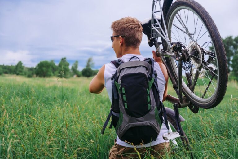 A cyclist carrying mountain bike on the meadow.